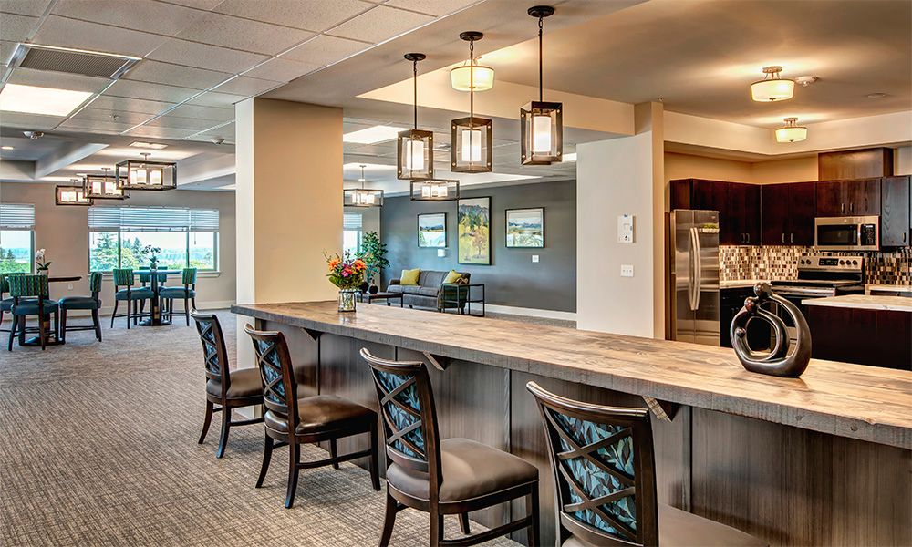 A modern kitchen interior with a long counter and stylish bar stools, illuminated by pendant lights.