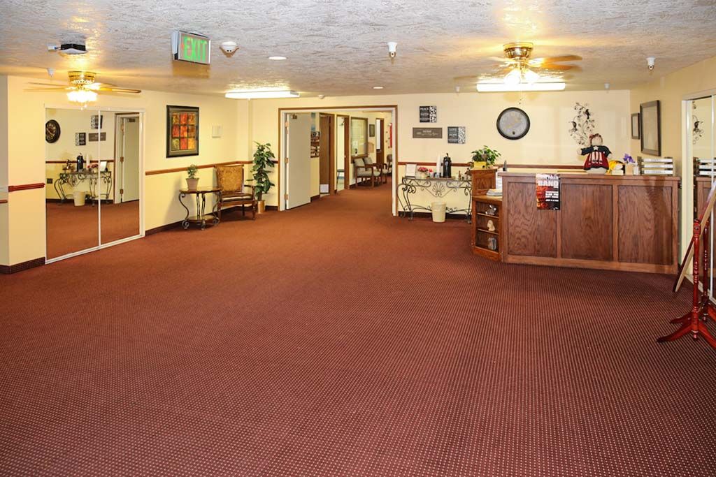 A spacious lobby with a carpeted floor, featuring a reception desk and hallway leading to various rooms.