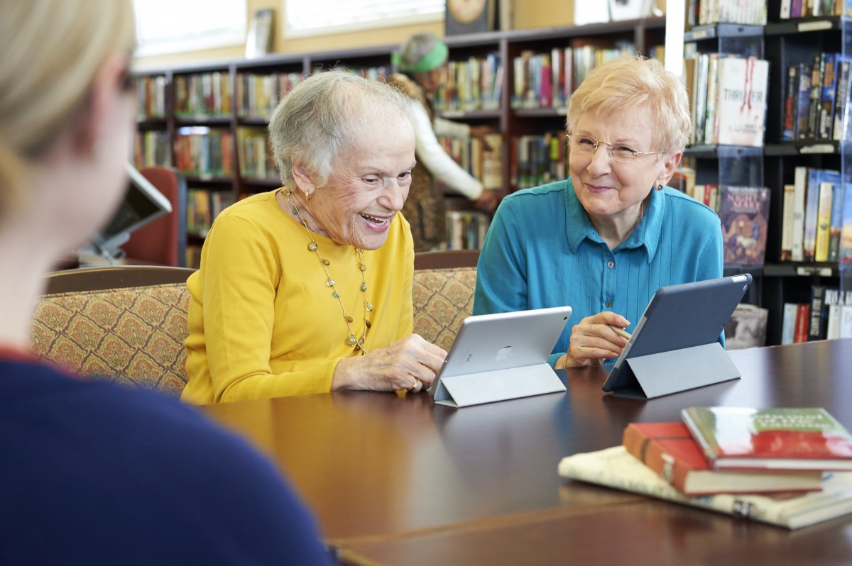 Two senior individuals using tablets in a library setting.