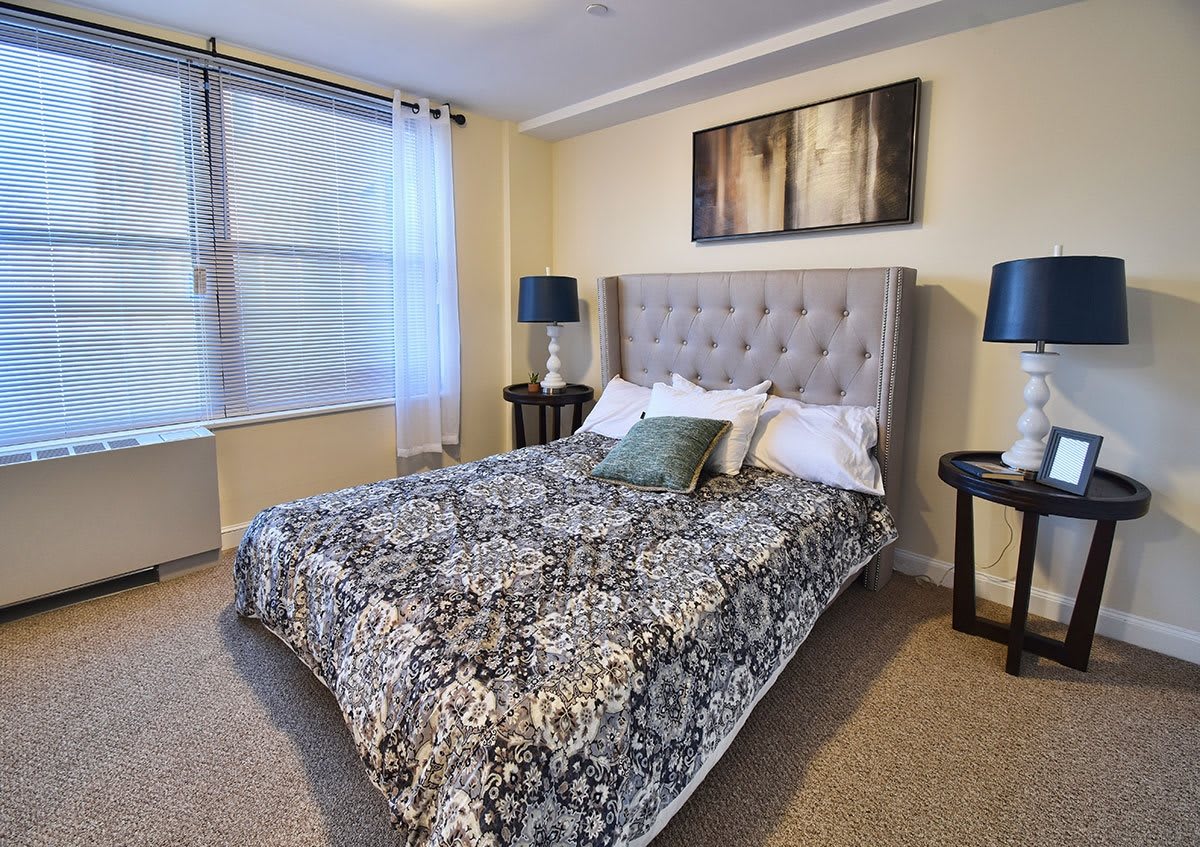 A cozy bedroom featuring a patterned bedspread, tufted headboard, and elegant nightstands with matching lamps.