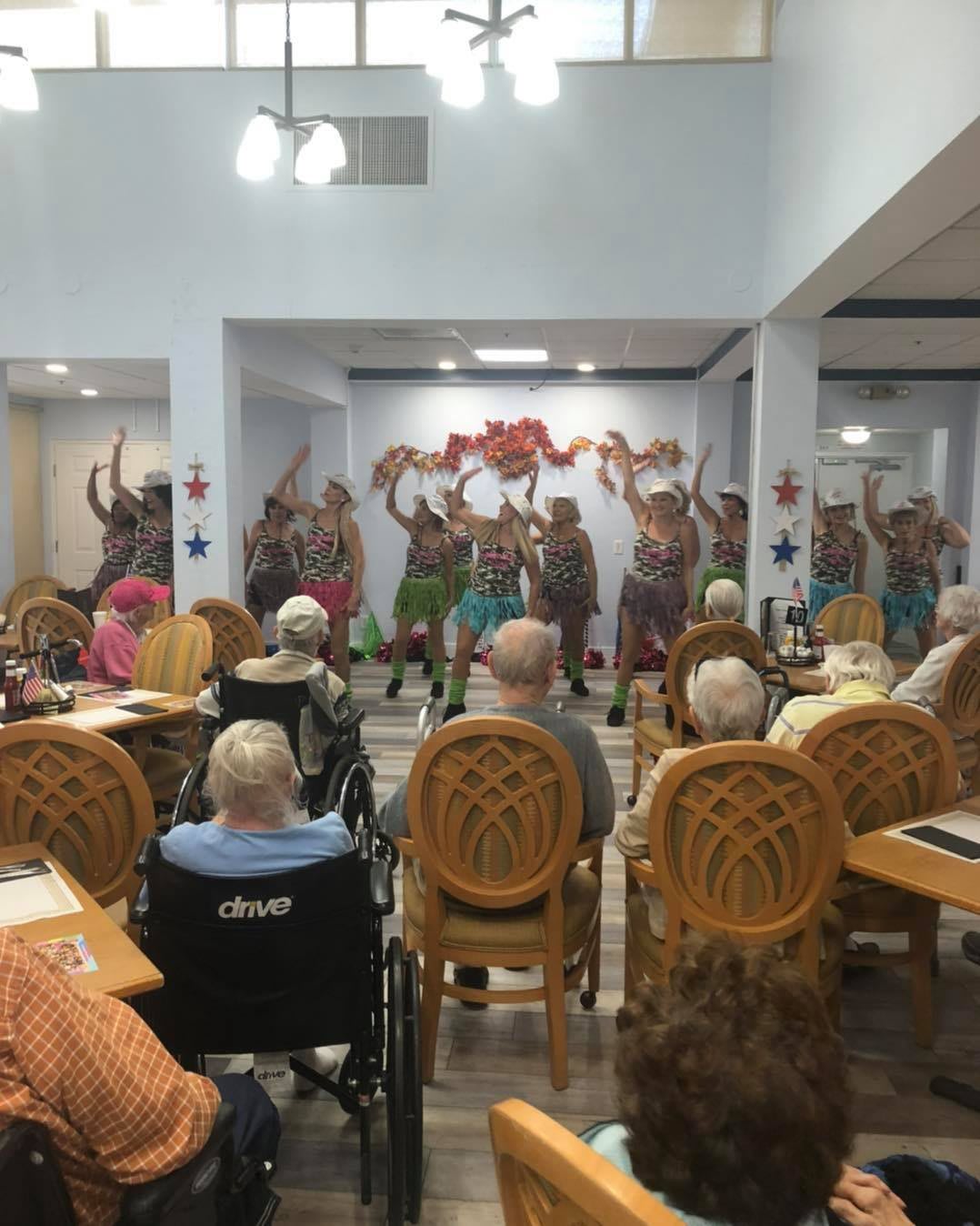 A group of dancers performs for an audience of seniors in an indoor setting.