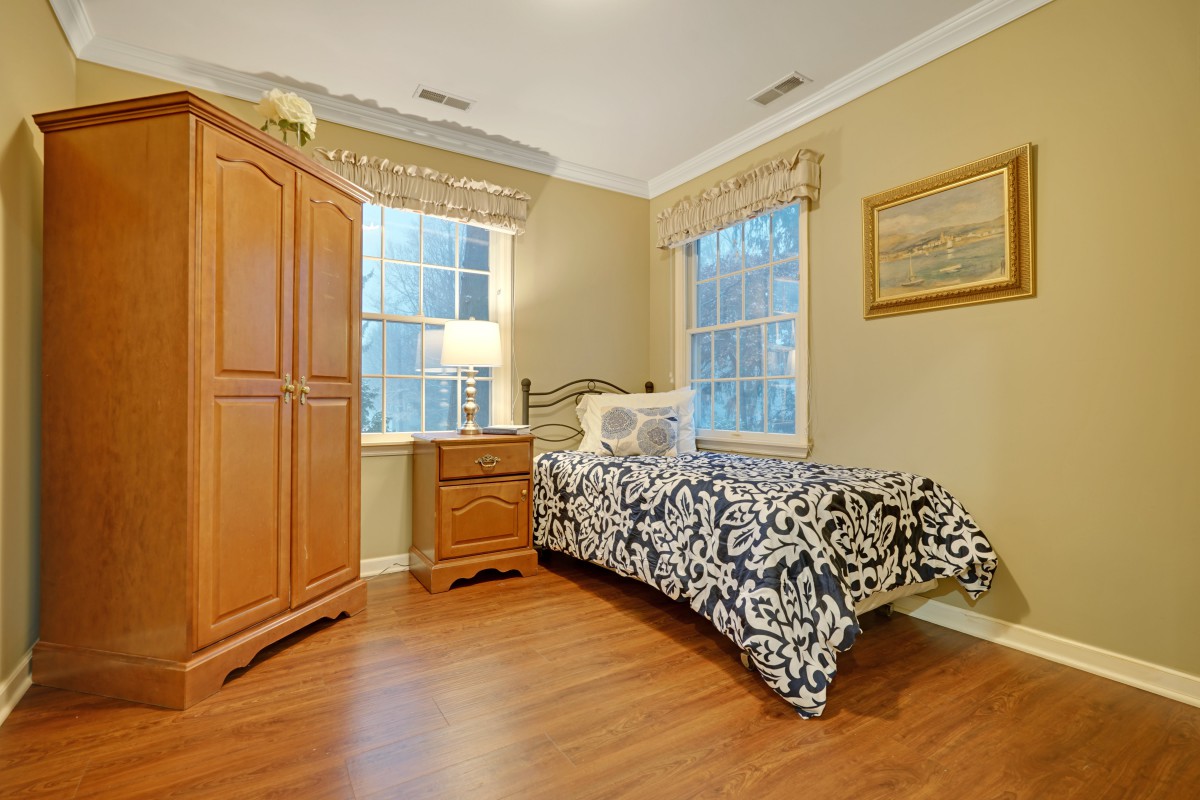A cozy bedroom with a single bed, wooden furniture, and large windows bringing in natural light.