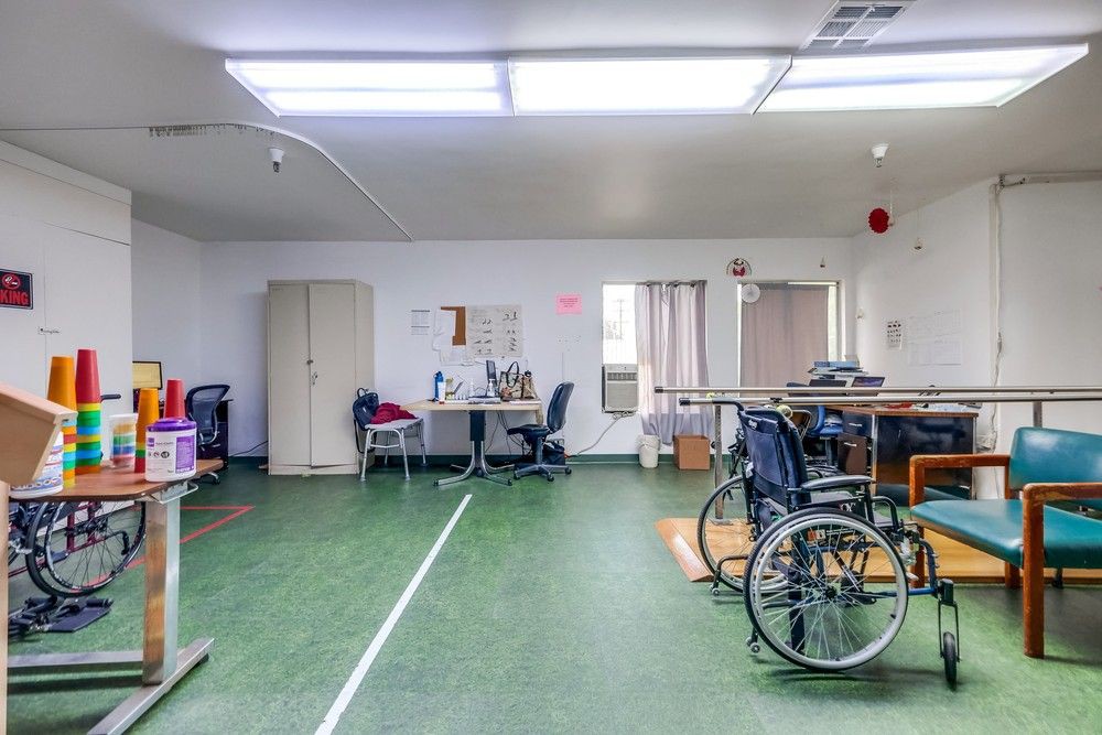 A spacious room equipped with wheelchairs, office chairs, tables, and other equipment.