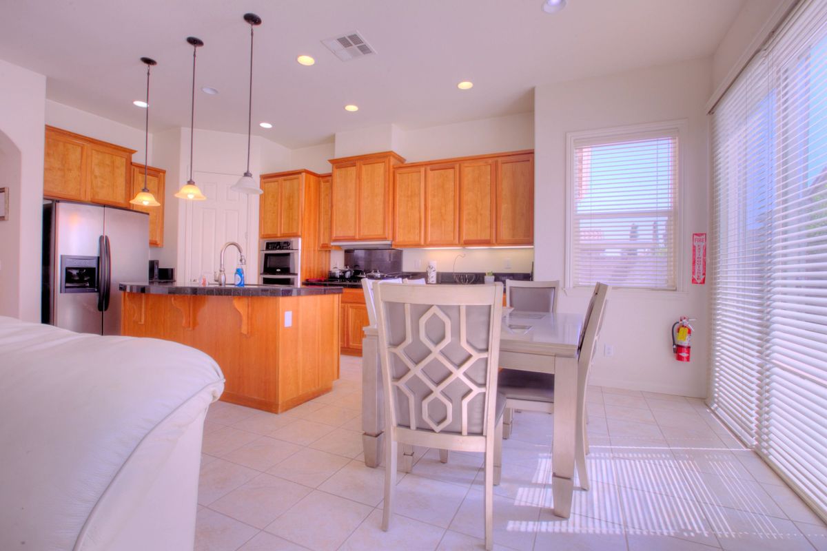 A modern kitchen with wooden cabinets and a dining area, featuring pendant lighting and bar stools.