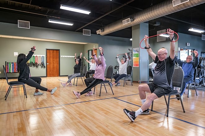 A group of senior citizens engaged in a chair-based exercise class indoors, focusing on health and fitness.