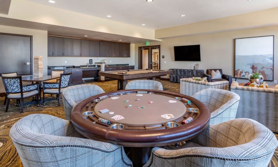 A spacious and modern game room featuring a poker table, comfortable seating, and a large television.