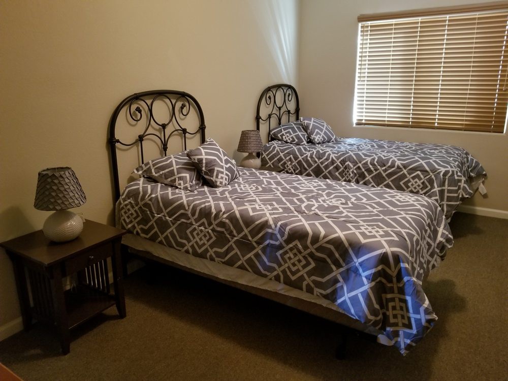 A cozy bedroom with two twin beds featuring patterned bedding, complemented by a small bedside table and a lamp.