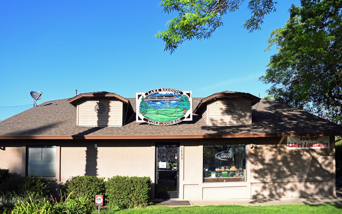 A small commercial building with a prominent sign and trees under a clear blue sky.