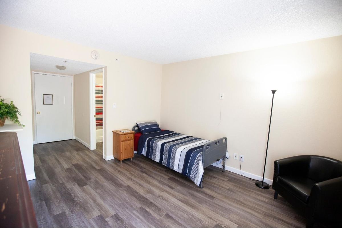 A minimalist bedroom featuring a single bed and a floor lamp on wooden flooring.