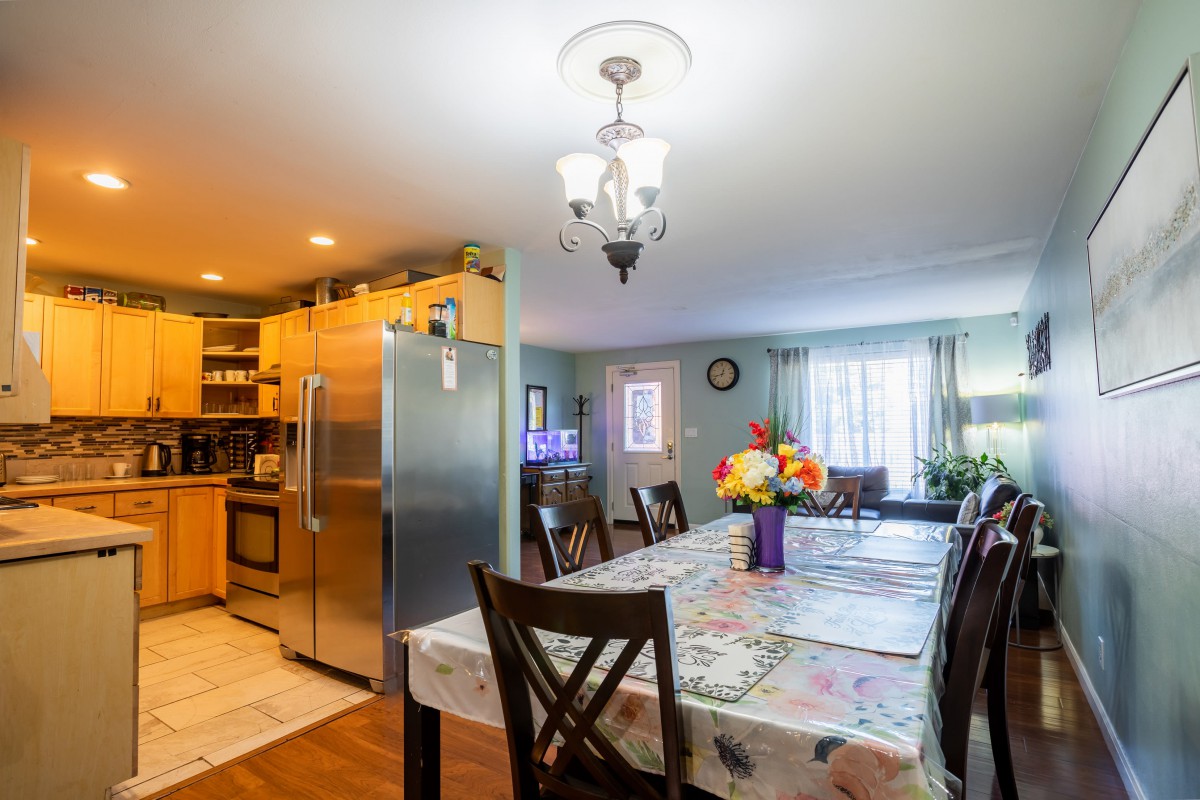 A cozy dining area with a table and chairs next to a modern kitchen, featuring a chandelier and floral centerpiece.