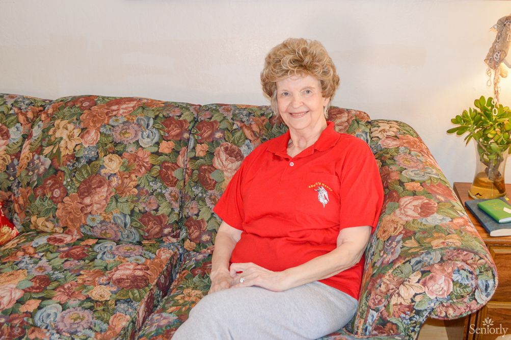 A woman sitting on a floral-patterned couch wearing a red shirt.