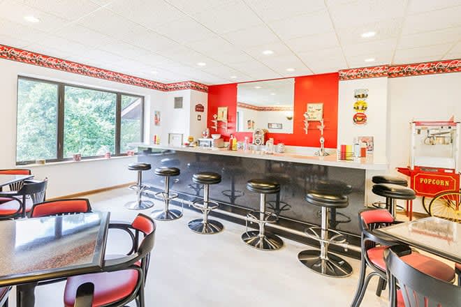 A retro-style diner interior featuring bar stools, a counter, and vibrant red and white decor.