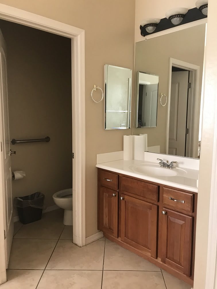 A clean and well-organized bathroom featuring a sink with a wooden cabinet, a mirror, and a toilet in an adjacent space.