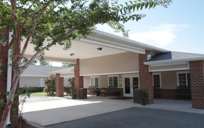 The image shows the entrance of a building with a covered driveway, surrounded by trees.