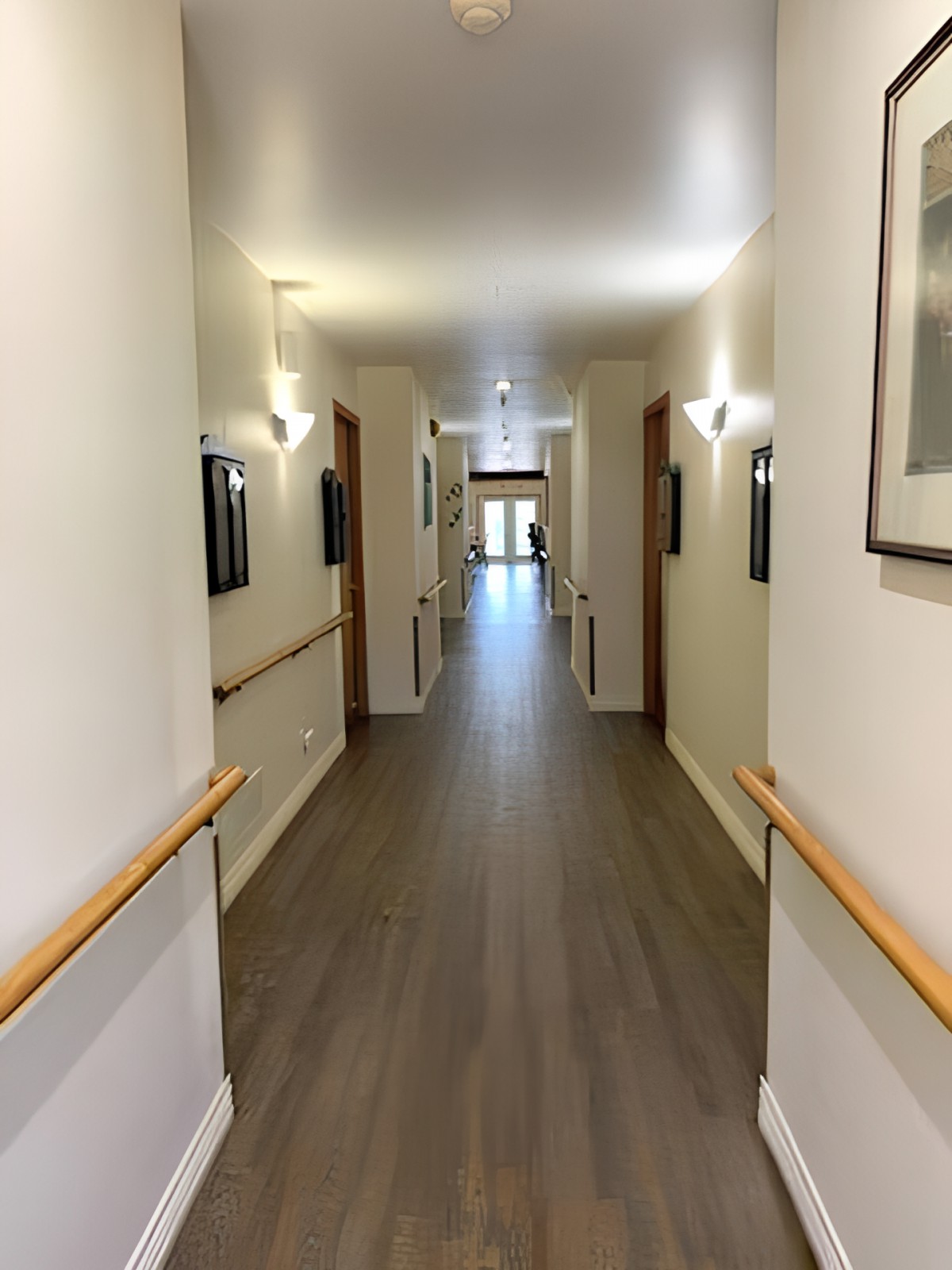A modern hallway with wooden floors and handrails, featuring several doors and soft lighting.