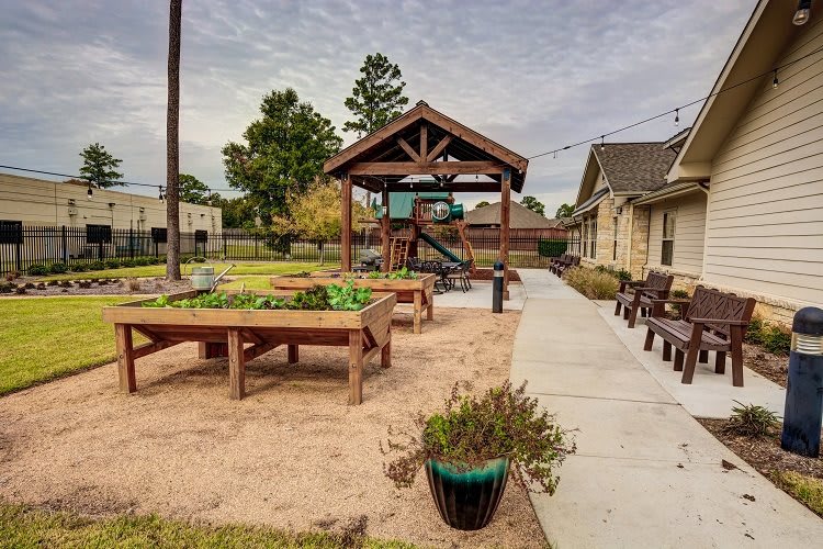 A community outdoor area featuring a playground, benches, and garden plots.