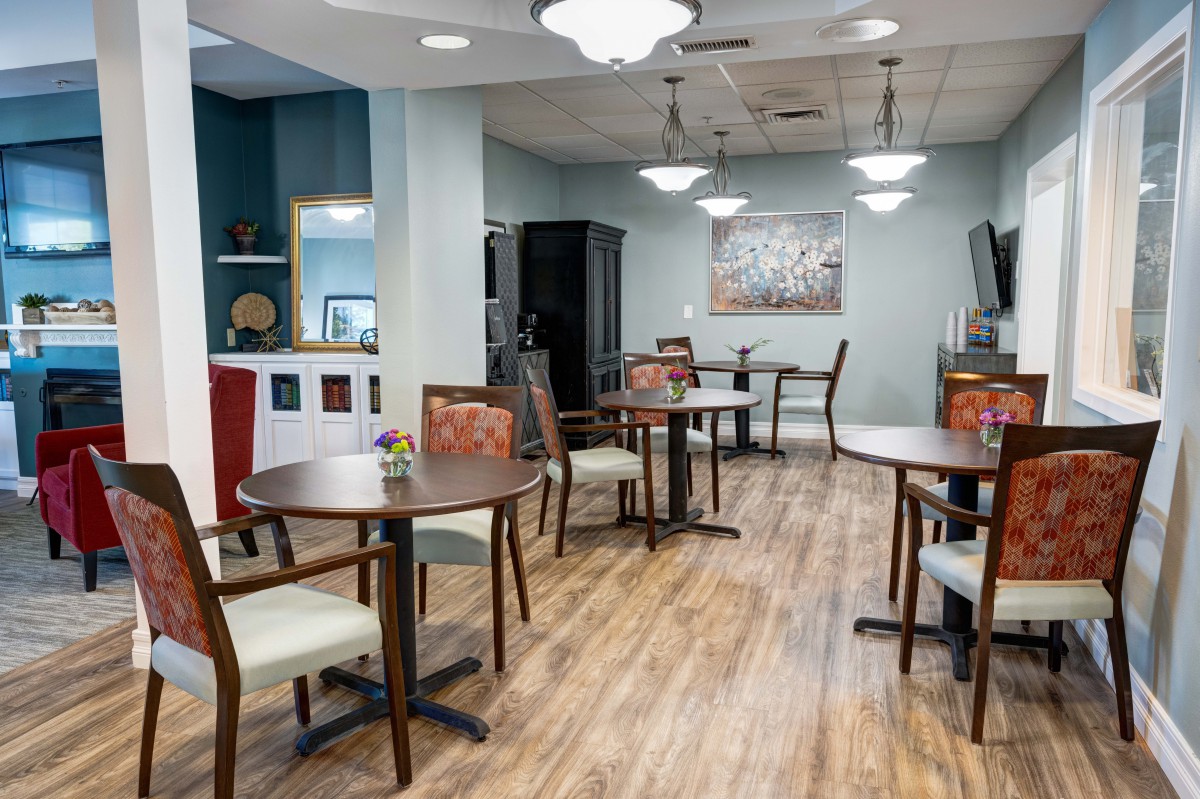 A modern dining area with neatly arranged tables and chairs, featuring elegant lighting and a wooden floor.