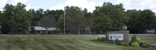 A building with an American flag on a lush green lawn, surrounded by trees under a clear sky.