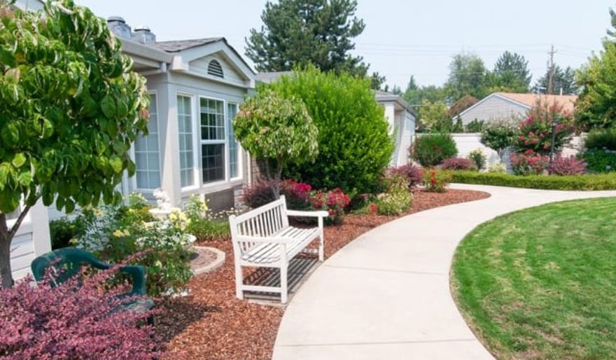 A well-maintained garden with a white bench and a curved pathway leading to a house.