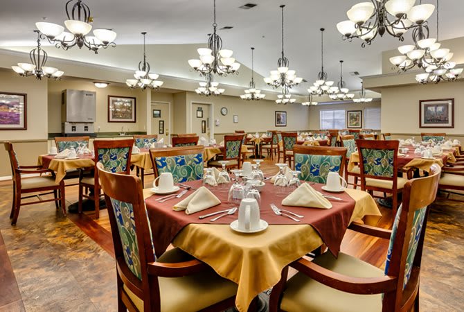 A well-decorated dining room with neatly arranged tables and chairs, featuring elegant chandeliers.