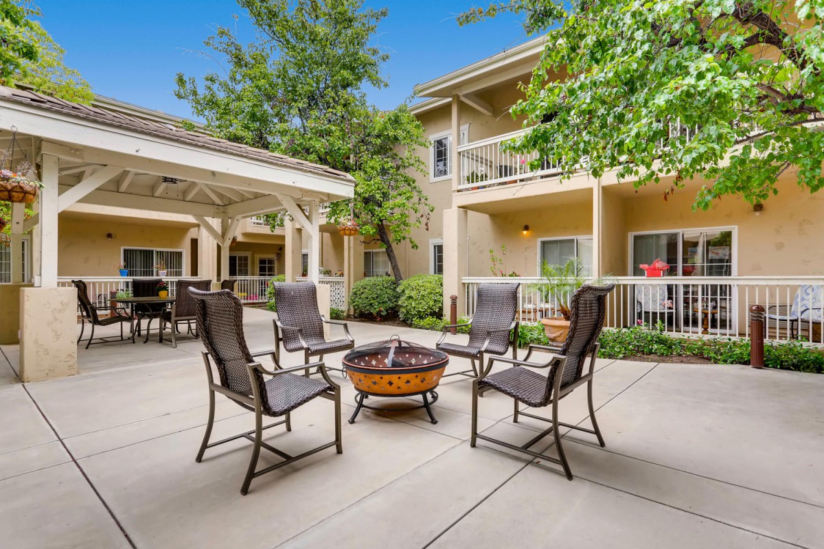 A cozy outdoor patio area with chairs arranged around a fire pit in an apartment complex courtyard.