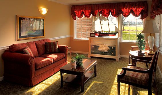 A cozy living room with a red sofa, wooden table, and a fireplace next to a large window.