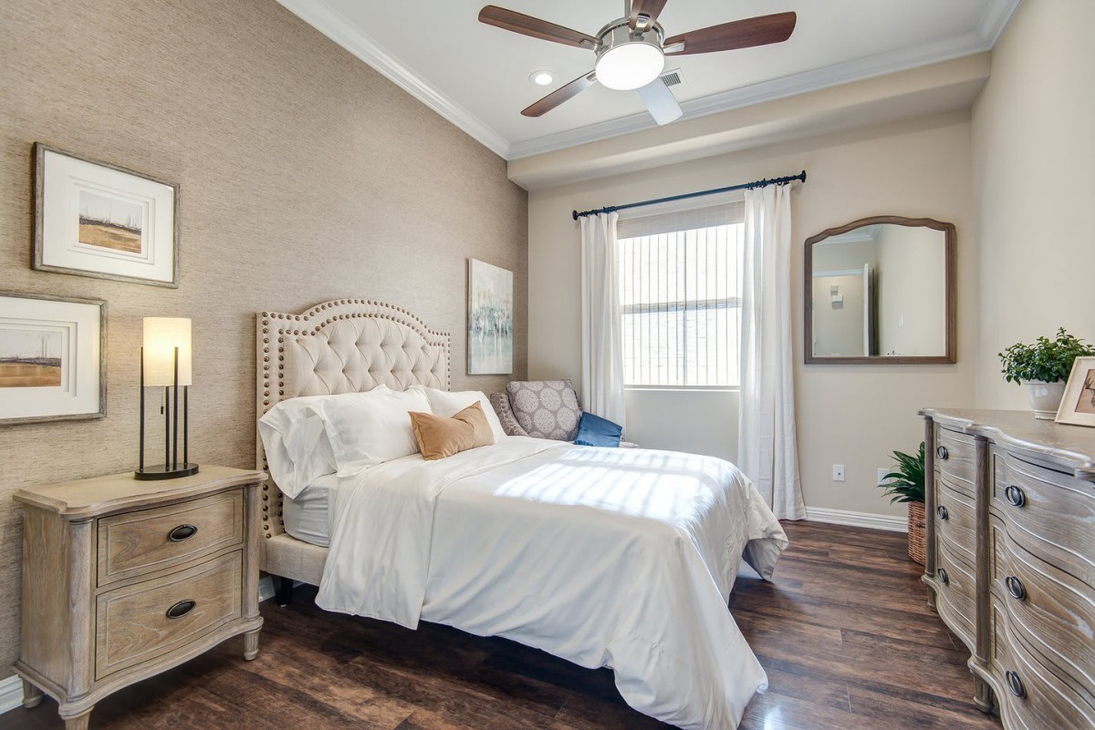 A cozy bedroom with a neatly made bed, wooden flooring, and a ceiling fan.