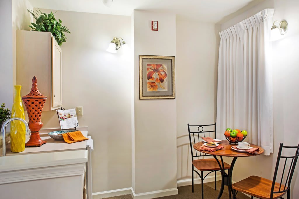 Cozy kitchen corner with a small dining table set for two, featuring a fruit bowl and wall art.