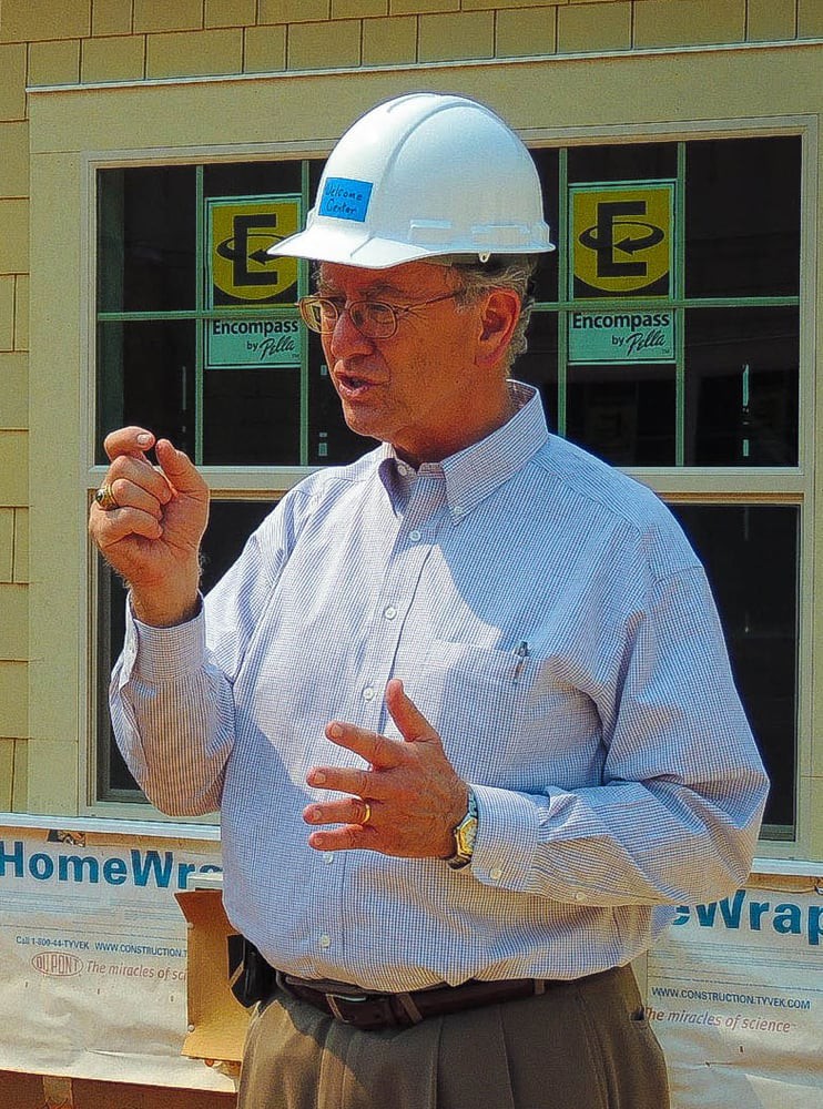 A construction worker wearing a hard hat gestures while speaking on-site.
