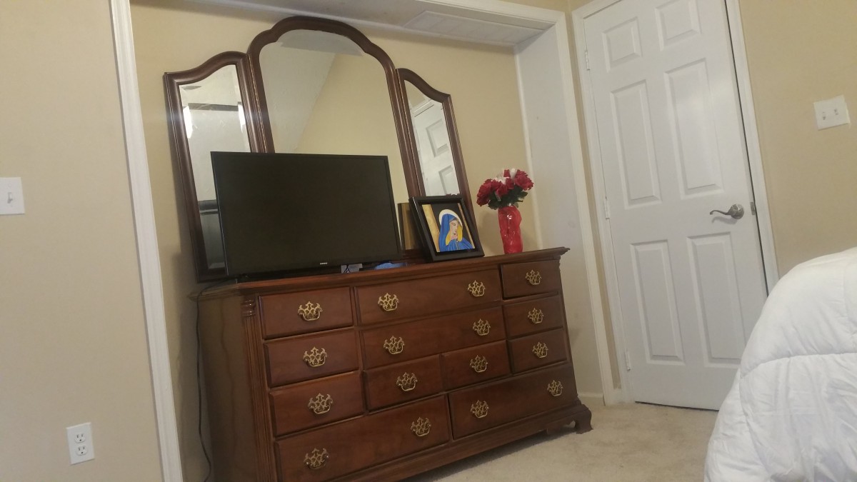 A bedroom dresser with a mirror, television, and a vase of flowers.