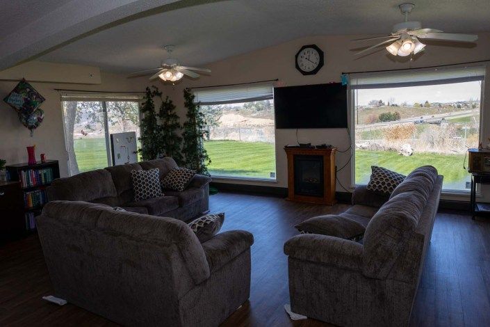 A cozy living room with large windows, featuring comfortable sofas, a television, and a fireplace.