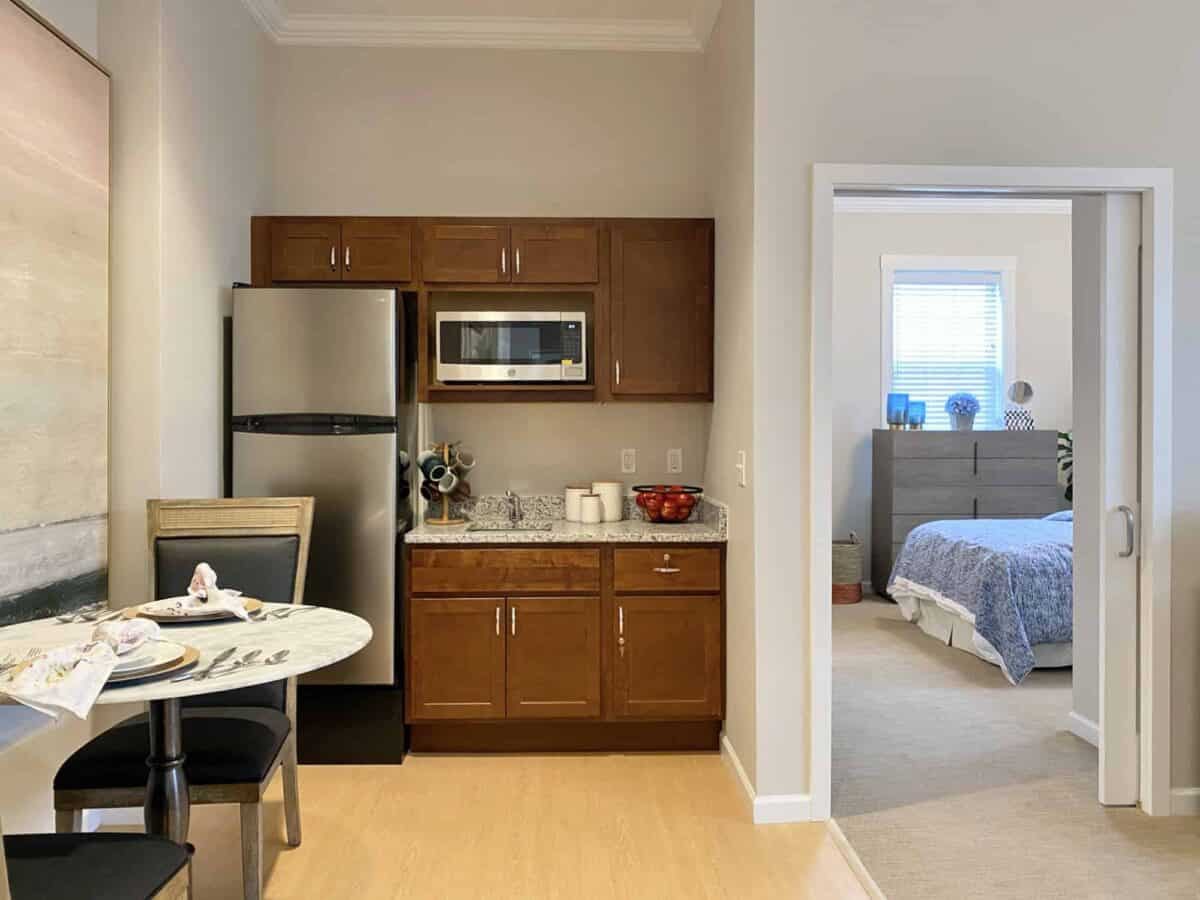 A compact kitchenette with a table in an apartment, adjoining a bedroom.