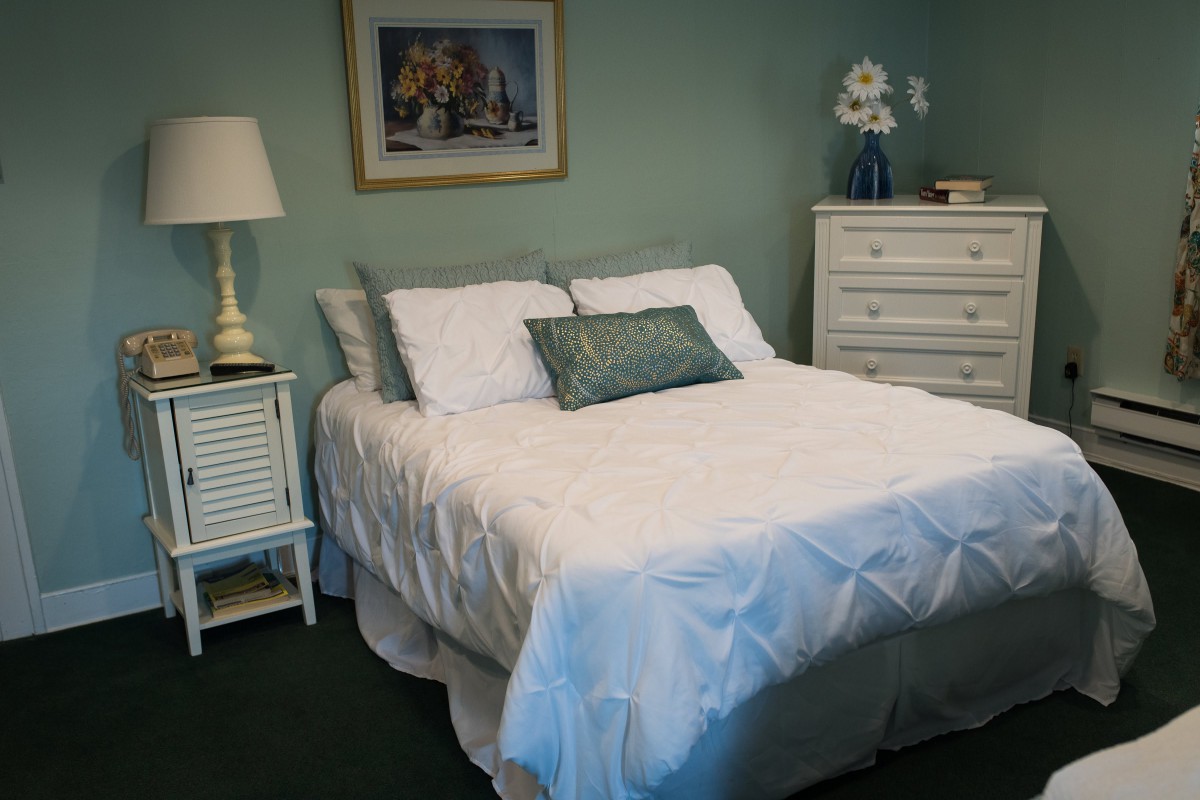 A cozy bedroom with a neatly made bed, a bedside lamp, and a dresser topped with decorative items.