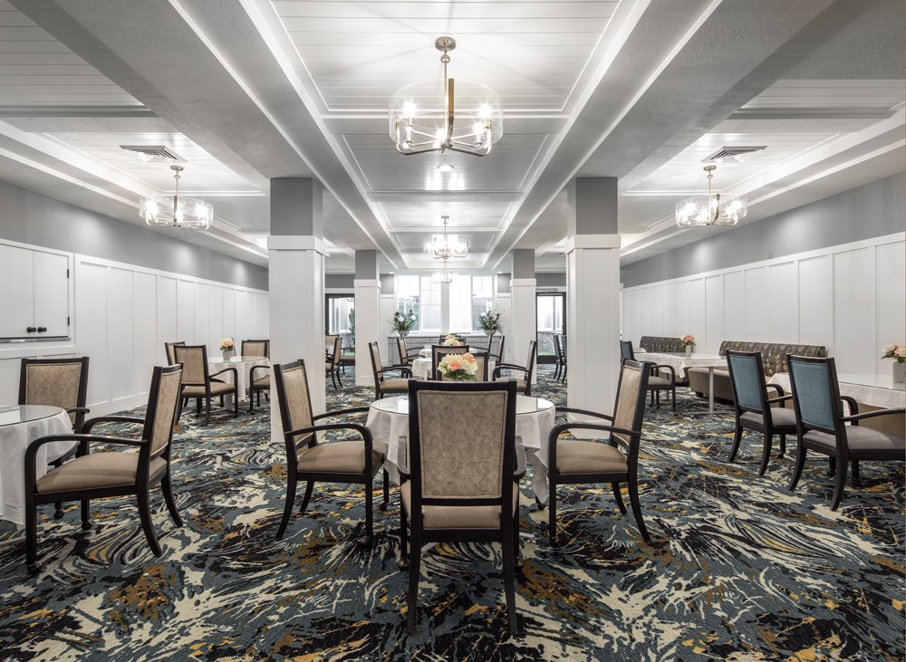 Elegant dining area with neatly arranged tables and chairs, featuring sophisticated lighting and patterned carpet.