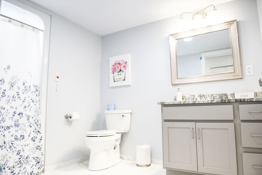 A clean and minimalist bathroom featuring a toilet, sink with vanity, mirror, and framed artwork.