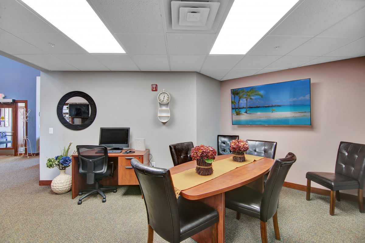 A small office meeting room with a conference table, chairs, and a computer desk.