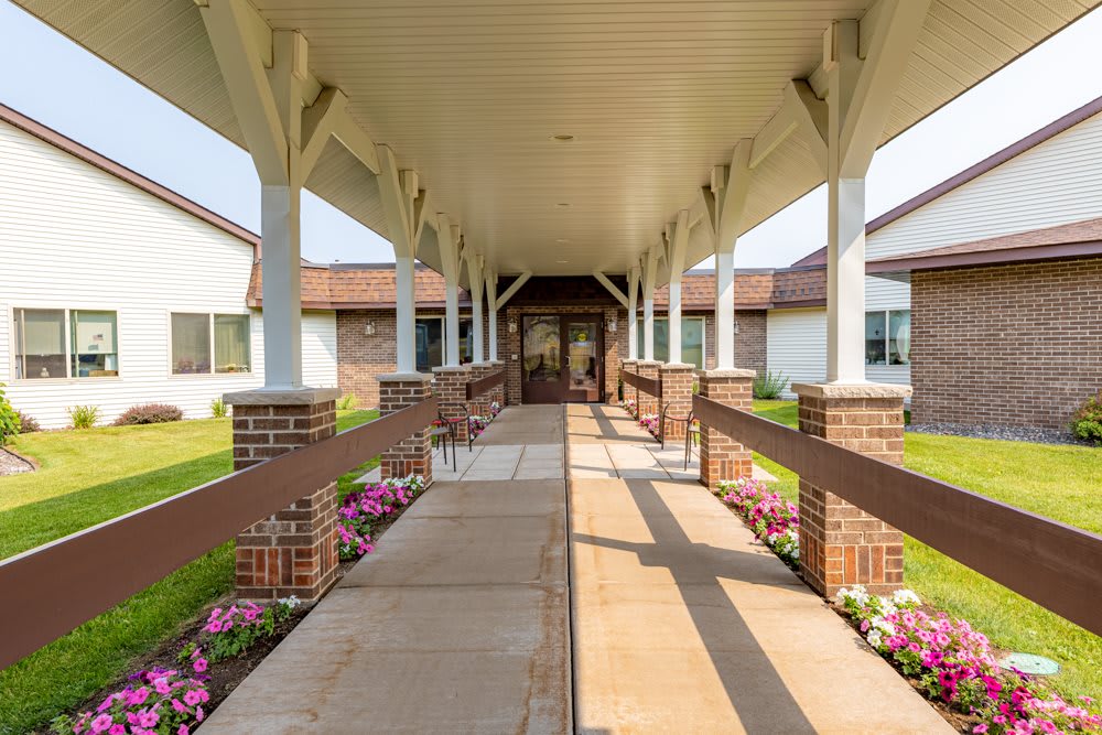 A covered walkway leads to the entrance of a building, flanked by flower beds.
