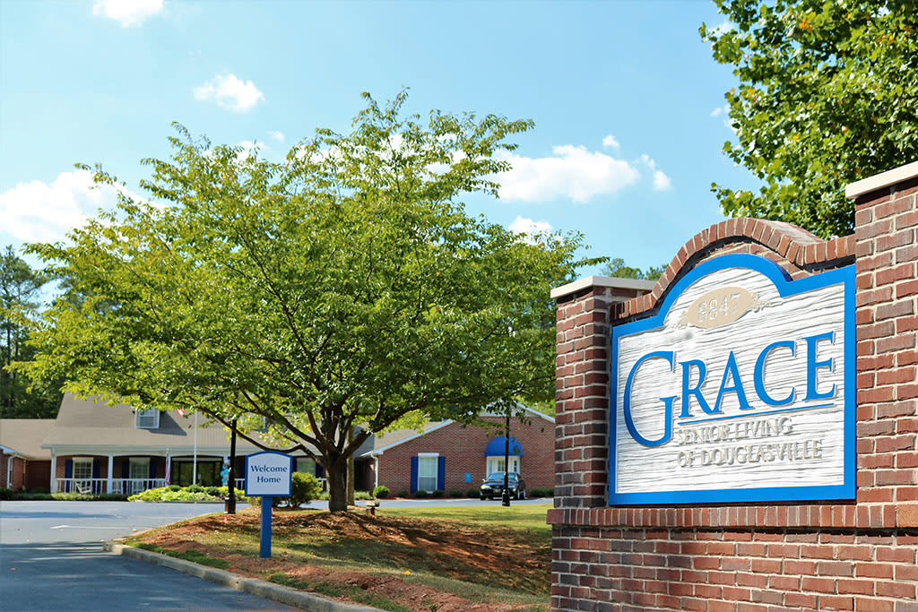 A view of a brick sign and nearby buildings surrounded by trees under a clear sky.