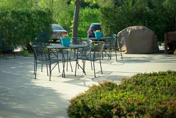 An outdoor patio area with metal chairs and tables, surrounded by greenery and parked cars.