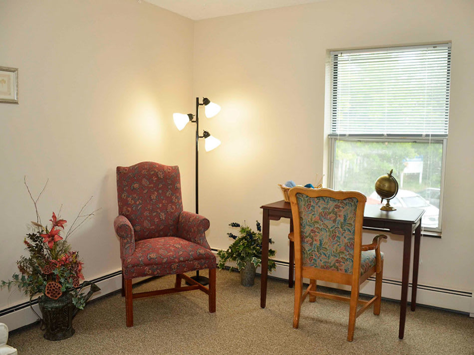 A cozy home office with a desk, two chairs, a lamp, and indoor plants by the window.