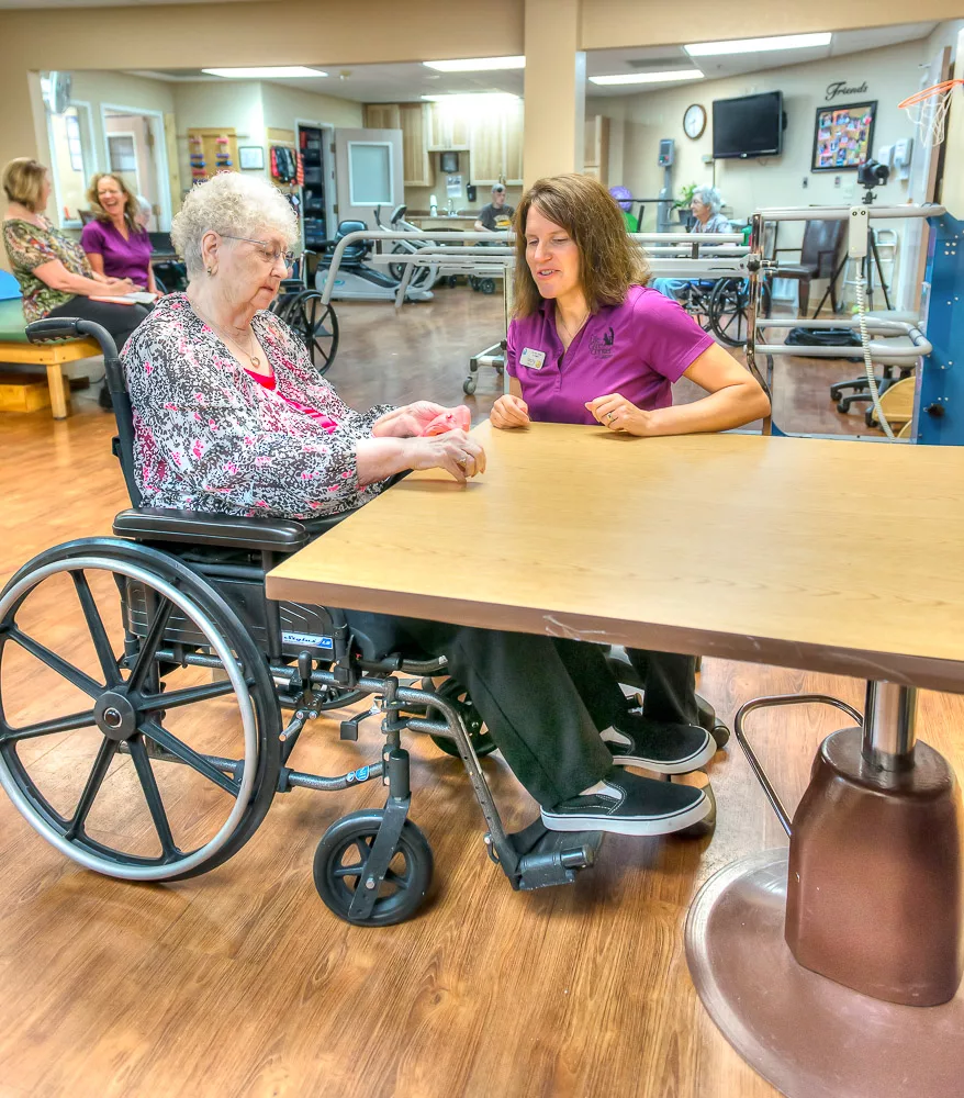 A caregiver assists an elderly person in a wheelchair at a nursing home.