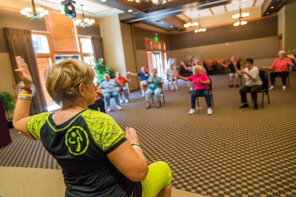 A group of seniors participating in an indoor fitness class led by an instructor.