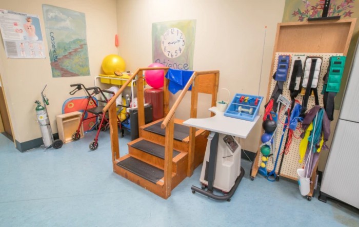 A physical therapy room equipped with exercise equipment, including a set of stairs, various balls, and mobility aids.
