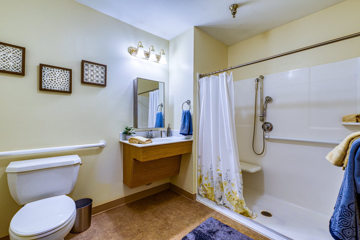 A clean and organized bathroom featuring a shower with curtain, sink with mirror, and a toilet.