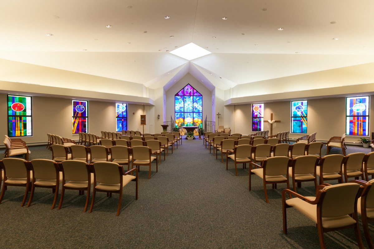 Interior view of a chapel with rows of chairs and colorful stained glass windows.