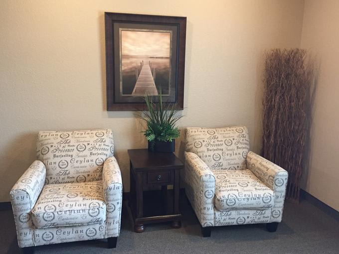 A cozy seating area with two patterned chairs, a side table, and artwork on the wall.