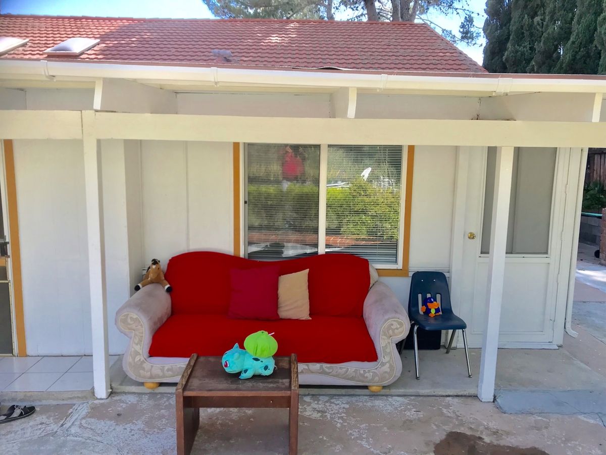 An outdoor patio area featuring a couch with a red cover, colorful pillows, and toys on a wooden table.