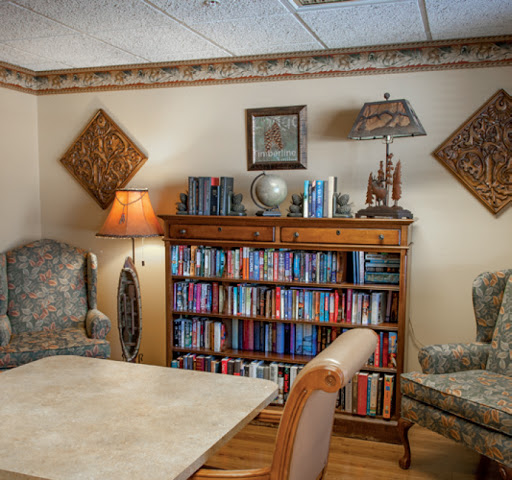 A cozy living room featuring a bookshelf filled with books, comfortable chairs, and warm lighting.