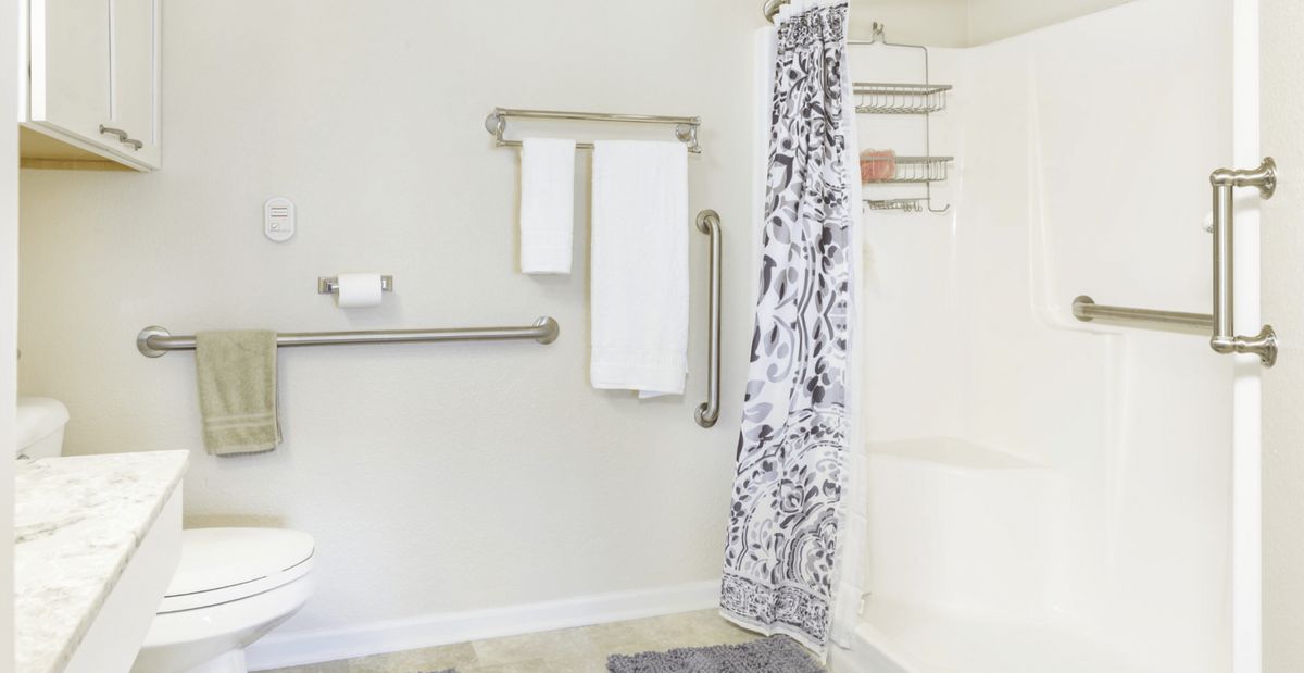 A bathroom with a shower area, decorative curtain, towel rack, and grab bars.