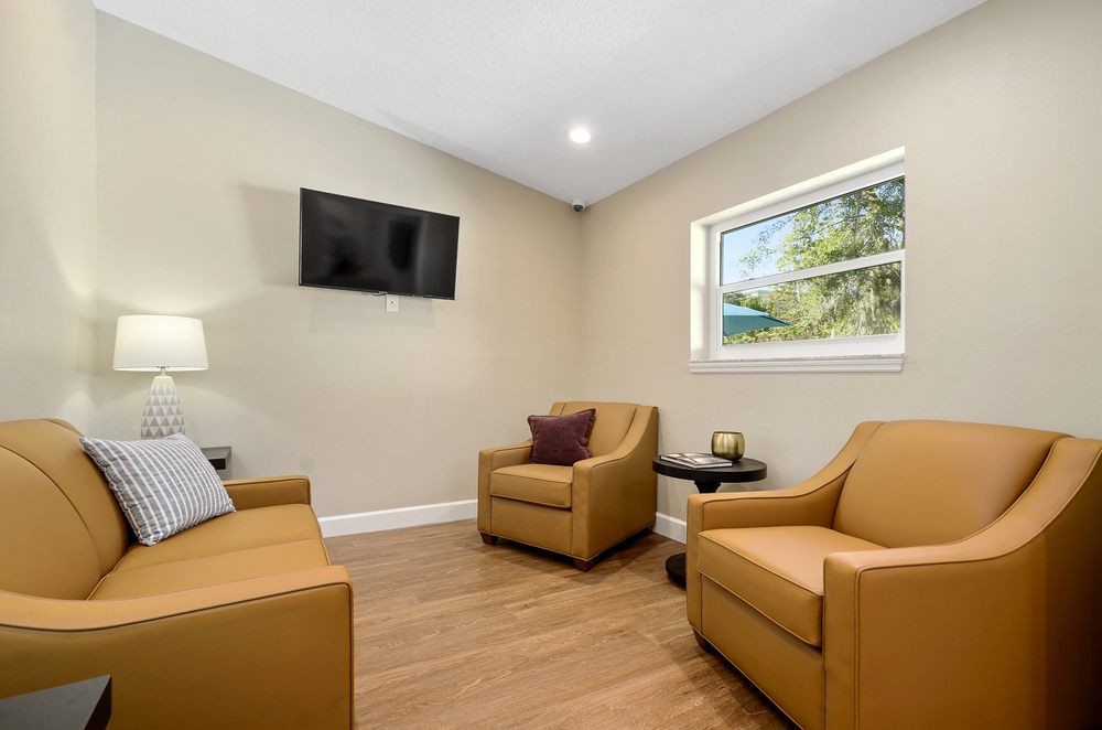 A cozy living room with two armchairs, a television mounted on the wall, and a window allowing natural light to fill the space.